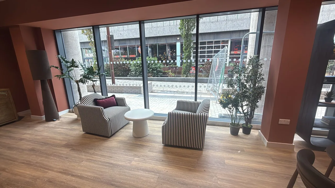 Communal seating area with upholstered chairs beside full-height windows.