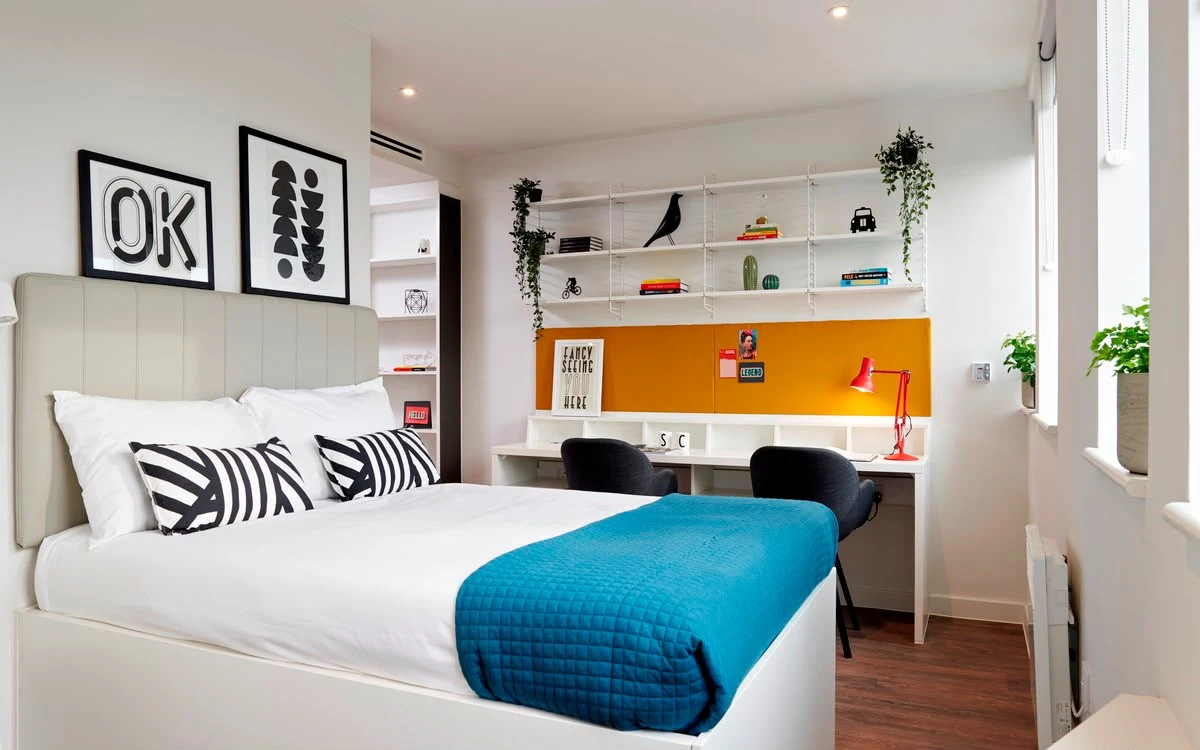 Furnished student bedroom with a bed, desks, shelving and storage.